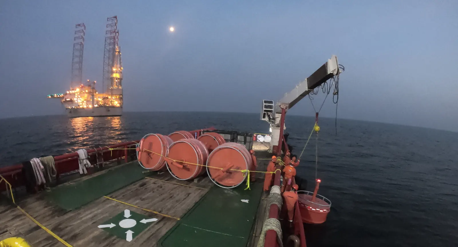 Boyas de señalamiento sobre la cubierta de una embarcación, con una plataforma iluminada al amanecer en el Golfo de México