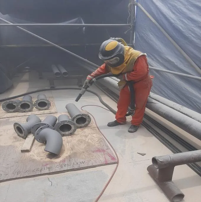 Operario aplicando sand-blast a piezas de tubería
